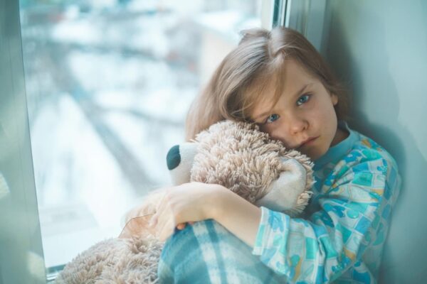 Child looking sad while holding stuffed bear