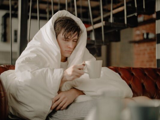 A sick young man covered in a blanket drinking tea