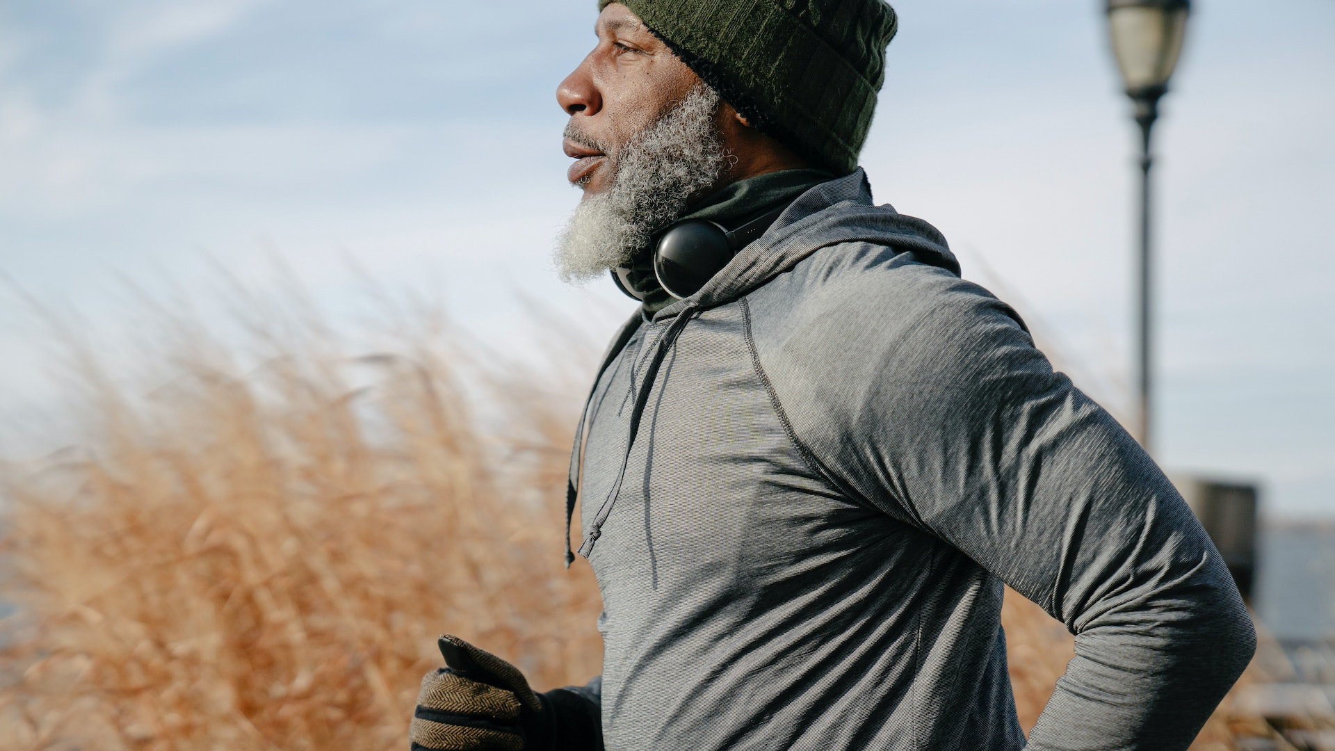 Black man with white beard in sportswear jogging in sunny autumn day