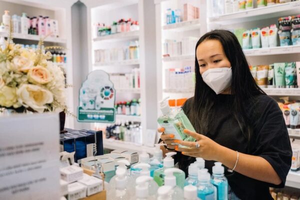Woman in a pharmacy with a mask over her mouth reads the label of a pharmaceutical product