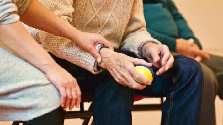 A zoom in photo of a person holding the arm of an elderly person that's holding a ball
