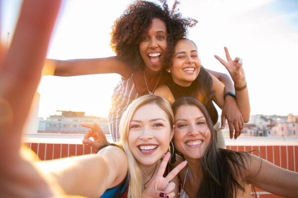 Cheerful friends capturing a fun selfie on a rooftop during sunset, enjoying a positive and trendy moment