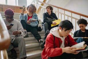 A group of students sits on a staircase. Some of them look at their phone, while others read.